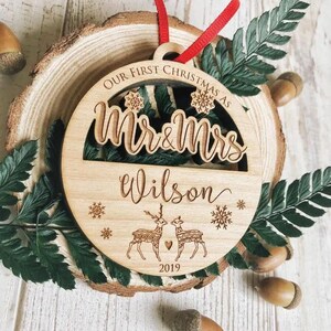 Puede incluir: Un adorno navide&ntilde;o de madera con el texto "Our First Christmas as Mr & Mrs Wilson 2019" y un dise&ntilde;o de dos renos con corazones.