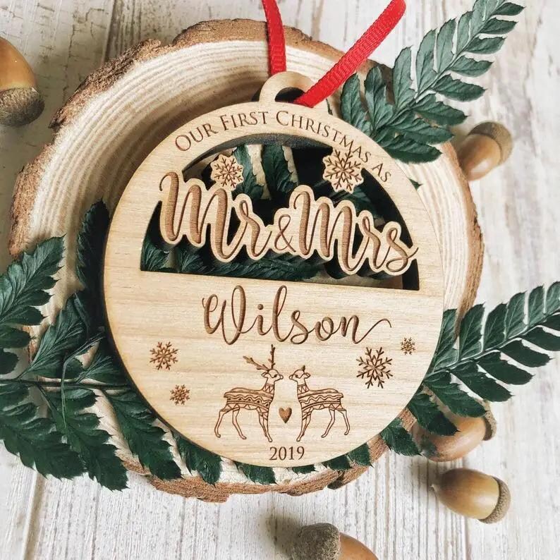 Puede incluir: Un adorno navide&ntilde;o de madera con el texto "Our First Christmas as Mr & Mrs Wilson 2019" y un dise&ntilde;o de dos renos con corazones.