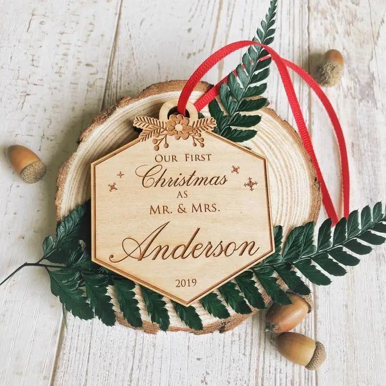 Puede incluir: Un adorno navide&ntilde;o de madera con el texto "Our First Christmas as Mr. & Mrs. Anderson 2019" en una fuente cursiva. El adorno est&aacute; decorado con un dise&ntilde;o floral y copos de nieve.