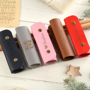 May include: Six personalized leather drum stick holders in various colors, including pink, brown, gray, blue, and red. Each holder has a different inscription, such as "Sophie", "D & M", "2024 12 220", "A Magic of Music", and "Happy Anniversary".