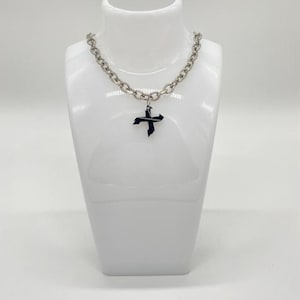 May include: Silver-coloured chain necklace with a black cross pendant. The necklace is displayed on a white mannequin bust. The cross pendant has a unique, angular design. The chain links are large and circular.