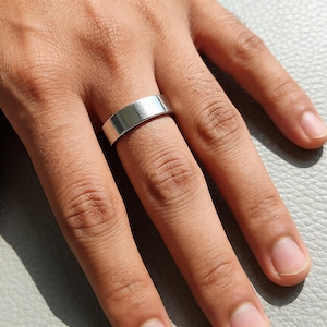 May include: A smooth, polished silver-toned band ring with a flat, wide profile and a reflective metallic surface. The ring features a simple, unadorned design with clean, straight edges, showcasing a uniform width around the entire circumference.