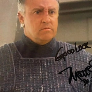 May include: A black and white photo of a man wearing a grey patterned shirt. The man is looking at the camera with a serious expression. The photo is signed "Good Luck" and "Terry D. Jones".