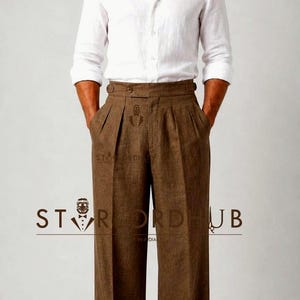 May include: A white long-sleeved button-down shirt paired with brown high-waisted trousers featuring double pleats, a wide waistband with side adjusters, and cuffed hems. The text "STORDHUB" is visible across the center of the trousers.