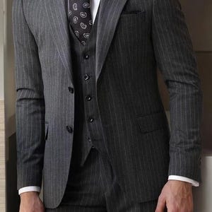Può includere: Un abito grigio a righe sottili con una cravatta a fantasia nera e una camicia bianca. Il vestito ha un gilet a tre bottoni.