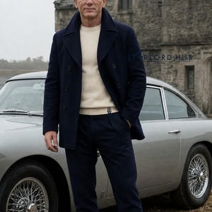 Peut inclure: Un homme porte un manteau bleu marine à double boutonnage, un pull crème et un pantalon bleu marine, à côté d'une voiture ancienne argentée. La scène se déroule en extérieur, avec un bâtiment en pierre en arrière-plan. L'esthétique générale est classique et sophistiquée.