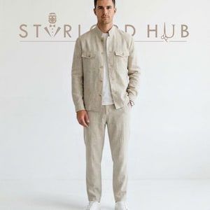 May include: A beige linen suit, consisting of a jacket and pants, paired with a white t-shirt and white sneakers. The jacket has two chest pockets and a mandarin collar. The background features the text "STORIARD HUB".