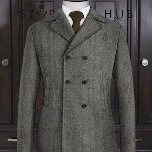 May include: A gray double-breasted coat with a herringbone pattern. The coat features a notched lapel, two rows of dark buttons, and a brown tie. The coat is displayed on a mannequin, with the text "STYLE HUB" visible.