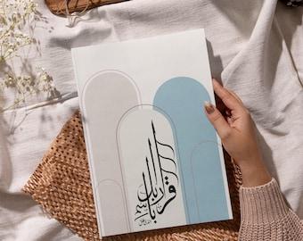 May include: A white book with a blue and gray abstract design. The book has Arabic calligraphy on the cover that reads "Wa Inna laka la al-akhira".