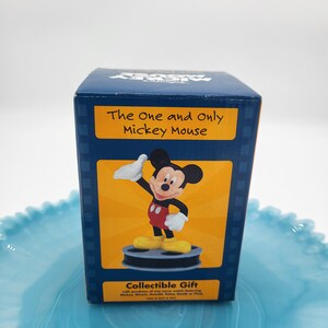 May include: A dark blue gift box with a Mickey Mouse figurine. The box has the text "The One and Only Mickey Mouse" on a yellow background. The figurine is in a classic pose, wearing red shorts and yellow shoes. A collectible gift.