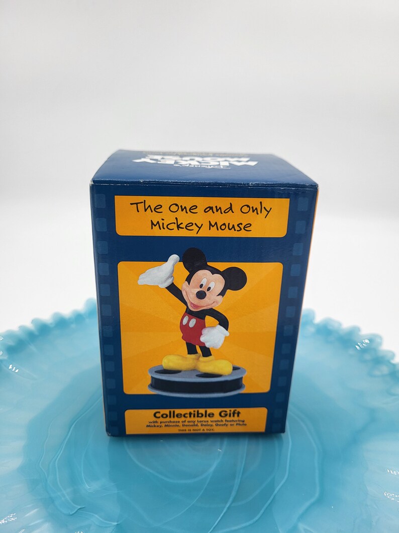 May include: A dark blue gift box with a Mickey Mouse figurine. The box has the text "The One and Only Mickey Mouse" on a yellow background. The figurine is in a classic pose, wearing red shorts and yellow shoes. A collectible gift.