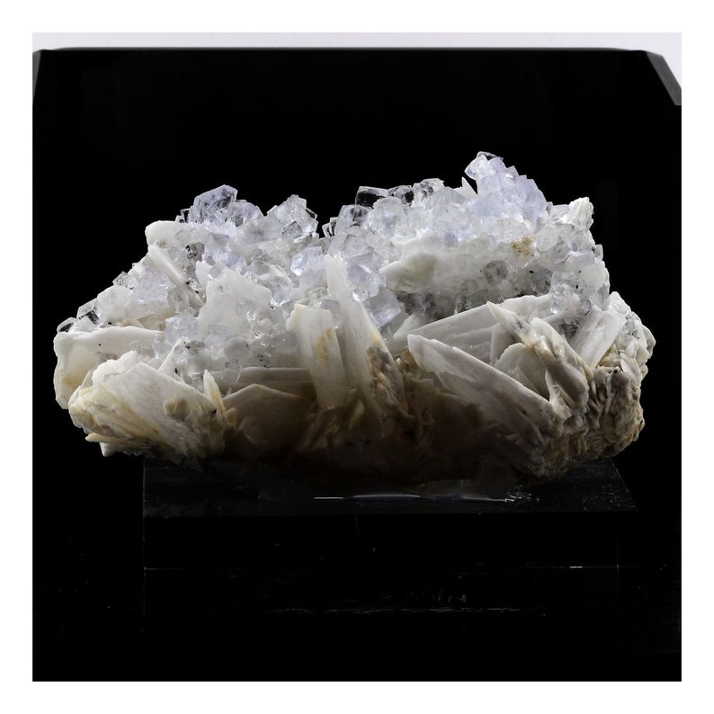 Puede incluir: Un grupo de cristales de barita blancos con cristales de fluorita transparentes en la parte superior. Los cristales est&aacute;n dispuestos en una forma natural y org&aacute;nica.