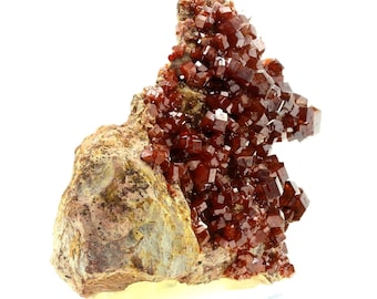 May include: A cluster of bright orange, cubic crystals on a rough, brown rock. The crystals are densely packed and have a glossy finish.