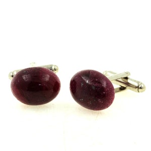 Può includere: Un paio di gemelli con pietre ovali, bordeaux scuro e finiture in metallo argentato. Le pietre hanno un aspetto marmorizzato, con venature più chiare nel colore di base più scuro. Su sfondo bianco.