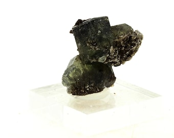 May include: A cluster of dark green mineral specimens, possibly tourmaline, on a clear, rectangular base. The crystals have a rough, textured surface and are set against a white background. The mineral appears to be naturally formed.