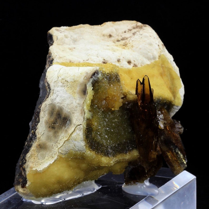 May include: A cluster of brown, needle-like crystals on a matrix of yellow and white calcite. The crystals are translucent and have a glassy lustre.