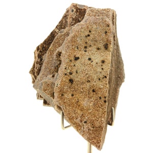 Könnte beinhalten: Geschichtetes Steinpräparat mit rauen Kanten, in Beige- und Brauntönen. Der Stein weist kleine, dunkle Flecken auf und wird auf einem Metallständer vor weißem Hintergrund präsentiert. Die Textur ist körnig.