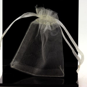 Puede incluir: Una bolsa de cordón blanco transparente hecha de tejido de malla. La bolsa está vacía y tiene un cordón blanco.