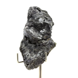 Può includere: Un esemplare di minerale grigio scuro, di forma irregolare e con lucentezza metallica. La roccia è montata su un supporto metallico argentato. La superficie è ruvida e strutturata, con strutture cristalline visibili.