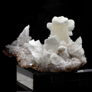 Peut inclure: Un groupe de cristaux de calcite blancs sur une matrice de calcite claire. Les cristaux sont translucides et présentent une variété de formes et de tailles. Le plus grand cristal est un cristal colonnaire haut et mince.