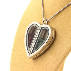 May include: Silver heart-shaped locket necklace with a clear glass front. The locket is divided into two sections, one filled with red stones and the other with green stones. A line of small clear crystals runs down the center.