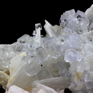 Puede incluir: Un grupo de cristales de fluorita c&uacute;bicos transparentes con un ligero tono p&uacute;rpura, anidados entre cristales de barita blancos. Los cristales de fluorita son transl&uacute;cidos y tienen un brillo v&iacute;treo.