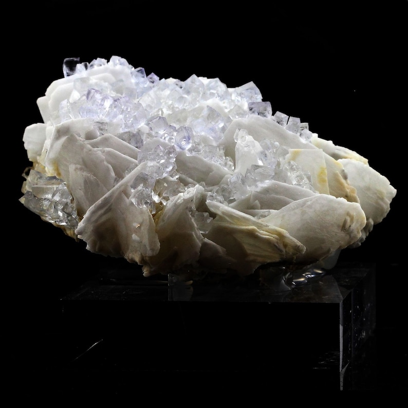 Puede incluir: Un grupo de cristales de barita blancos con una capa de cristales de fluorita claros y de color p&uacute;rpura claro en la parte superior. Los cristales est&aacute;n dispuestos en una forma natural y org&aacute;nica.