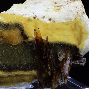 May include: A cluster of brown, translucent crystals set against a yellow, orange, and green background. The crystals are sharp and pointed, and they are arranged in a cluster. The background is a mix of yellow, orange, and green, and it is made up of smaller crystals.