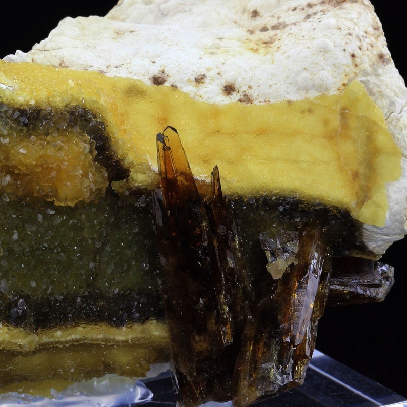 May include: A cluster of brown, translucent crystals set against a yellow, orange, and green background. The crystals are sharp and pointed, and they are arranged in a cluster. The background is a mix of yellow, orange, and green, and it is made up of smaller crystals.