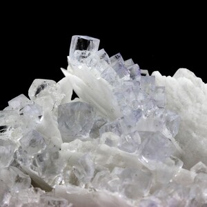 Puede incluir: Un grupo de cristales transparentes y transl&uacute;cidos con un tono ligeramente p&uacute;rpura. Los cristales est&aacute;n dispuestos en un patr&oacute;n aleatorio y se colocan sobre un fondo negro.