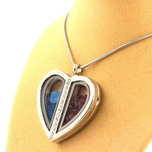 May include: Silver heart-shaped locket necklace with a clear glass front. The locket is divided into two sections, one filled with blue stones and the other with red stones. A line of small clear stones runs down the center of the locket.