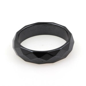 Könnte beinhalten: Ein schwarzer, facettierter Ring aus poliertem Metall. Der Ring hat ein geometrisches Design mit mehreren Facetten.