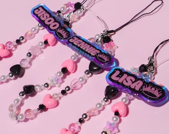 May include: Three colorful phone charms with black and white beads, pink hearts, and silver stars. Each charm features a holographic name tag with a crown: "JISOO", "JENNIE", and "LISA".