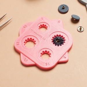 May include: A pink plastic tool with five different sized circles for setting snaps. The tool is labeled "STEFANJIRK CZ".