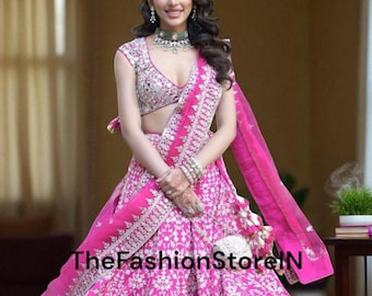 May include: A vibrant pink lehenga with intricate white embroidery and mirror work. The outfit includes a matching dupatta and a heavily embellished top. The text "TheFashionStoreIN" is visible on the skirt.