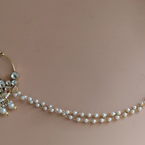 May include: A gold nose ring with a pearl chain. The nose ring is decorated with white stones and pearls.
