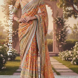 Op de afbeelding: Een ingewikkeld ontworpen sari in tinten oranje, geel en groen, met gedetailleerd borduurwerk en een contrasterende blauwe rand. De stof drapeert elegant en toont een traditioneel Indiaas kledingstuk. De tekst "TheFashionStoreIN" is zichtbaar.