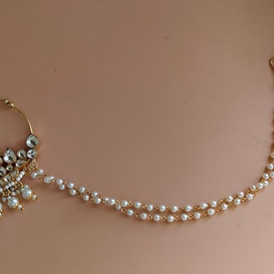 May include: A gold nose ring with a large, ornate design featuring white pearls and clear stones. A delicate chain with white pearls hangs from the ring.