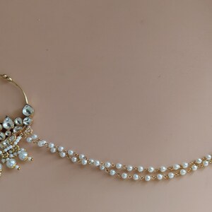 May include: A gold nose ring with a pearl chain. The nose ring is decorated with white stones and pearls. The chain is made of gold and pearls.