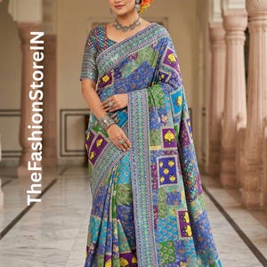 May include: A vibrant blue saree with a patchwork design featuring purple, yellow, and green squares. The saree has a detailed border and is adorned with intricate patterns. The text "TheFashionStoreIN" is visible on the left side.