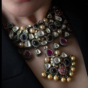 Puede incluir: Un collar de oro de varias capas con un gran colgante que presenta una variedad de piedras preciosas, incluyendo perlas, esmeraldas, rubíes y zafiros. El collar está decorado con detalles intrincados y un acabado de esmalte verde.