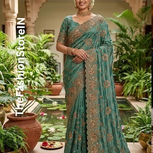 Peut inclure: Un sari turquoise avec des broderies et des ornements dorés. Le sari présente un motif floral détaillé sur les bordures et sur le tissu. Le texte "TheFashionStorelN" est visible sur le côté gauche de l'image.