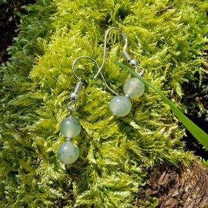 May include: A pair of silver earrings with green glass beads. The earrings are on a bed of green moss.