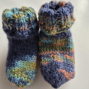 Könnte beinhalten: Ein Paar gestrickte Babyschuhe in blau, grün und orange Streifen. Die Schuhe haben einen umgeschlagenen Bund und sind aus weichem Garn gefertigt.