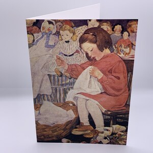 May include: A greeting card featuring a vintage-style illustration of a child in a red dress sitting on a wooden chair, sewing a white cloth. A woven basket filled with fabric sits on the floor, while several dolls are arranged in the background.
