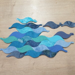 May include: A patchwork of blue, teal, and aqua fabric pieces sewn together in a wavy pattern, resembling ocean waves.