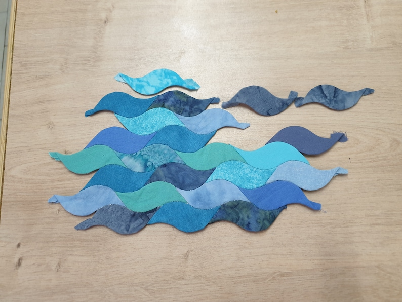May include: A patchwork of blue, teal, and aqua fabric pieces sewn together in a wavy pattern, resembling ocean waves.