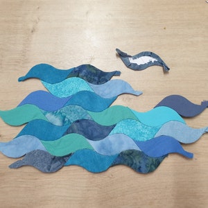 May include: A patchwork of blue, teal, and green fabric pieces sewn together in a wavy pattern, resembling ocean waves. The fabric pieces are arranged in a staggered pattern, creating a dynamic and textured look.
