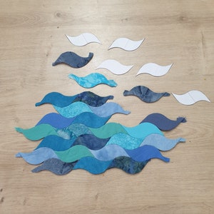 May include: A blue and green fabric wave pattern quilt block with white paper templates for sewing.