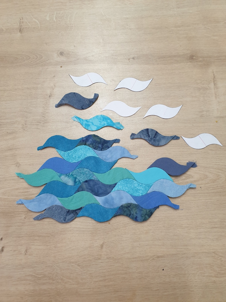 May include: A blue and green fabric wave pattern quilt block with white paper templates for sewing.